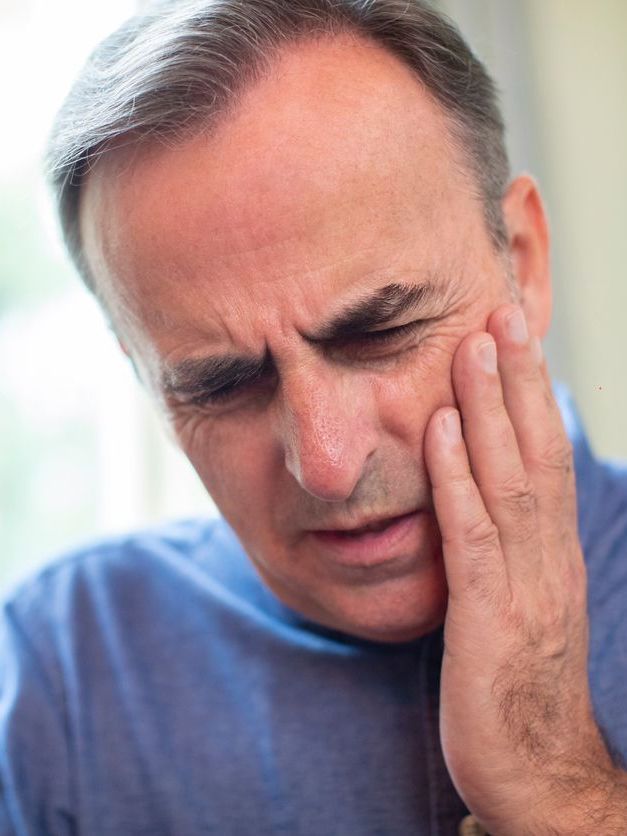 A man is holding his face in pain because he has a toothache.