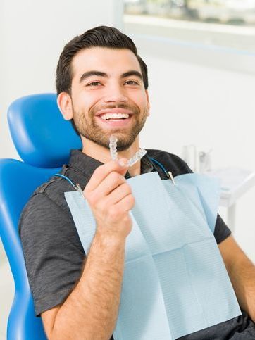 A man is sitting in a dental chair holding a clear braces.