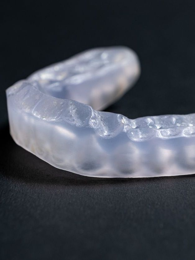 A close up of a clear mouth guard on a black surface.