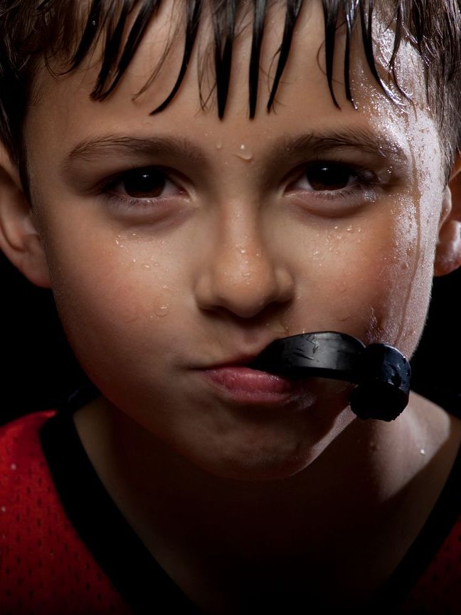 A young boy with a mouth guard in his mouth is sweating.