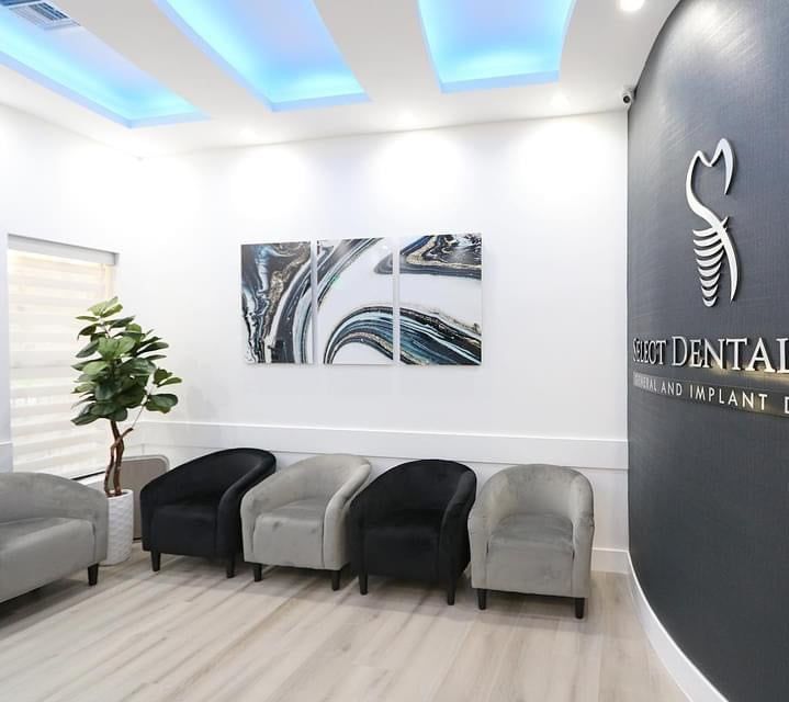 A waiting room at a dental office with chairs and a plant.