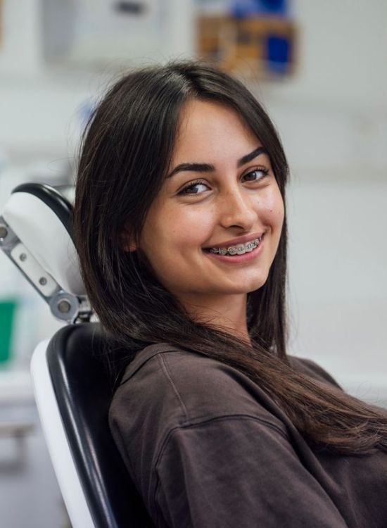 A woman with braces is smiling while sitting in a dental chair.