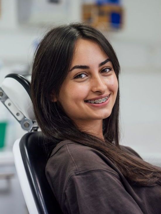 A woman with braces is smiling while sitting in a dental chair.