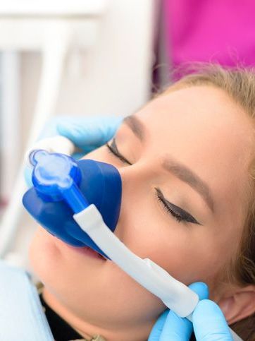 A woman is wearing an oxygen mask in a dental chair.