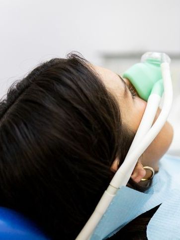 A woman is laying in a dental chair with an oxygen mask on her face.