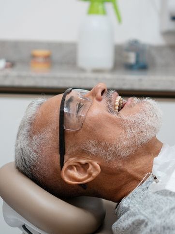 An older man is laying in a dental chair with his mouth open.