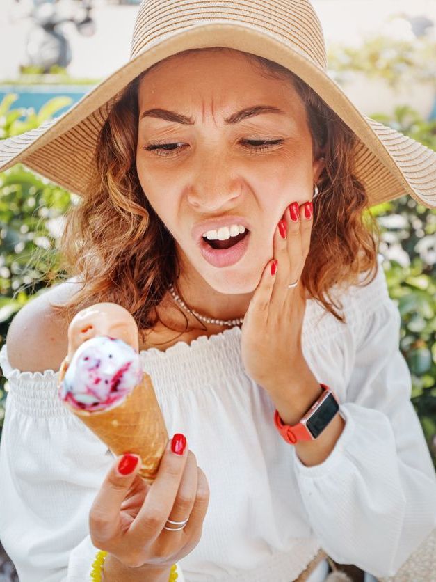 A woman in a hat is holding an ice cream cone and making a funny face.