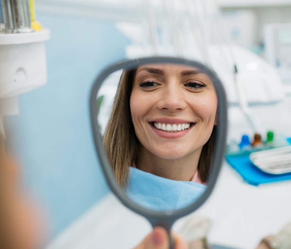 A woman is smiling in a hand mirror at the dentist.