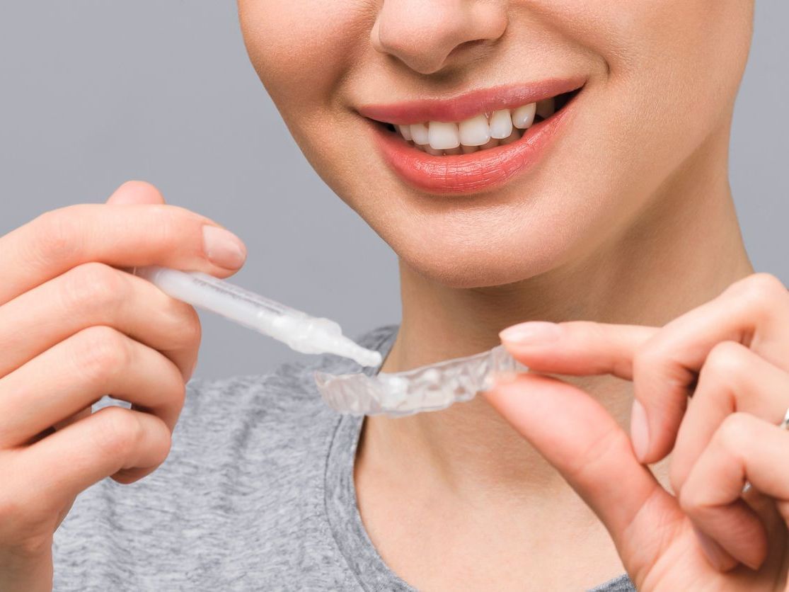 A woman is holding a whitening device in front of her mouth.