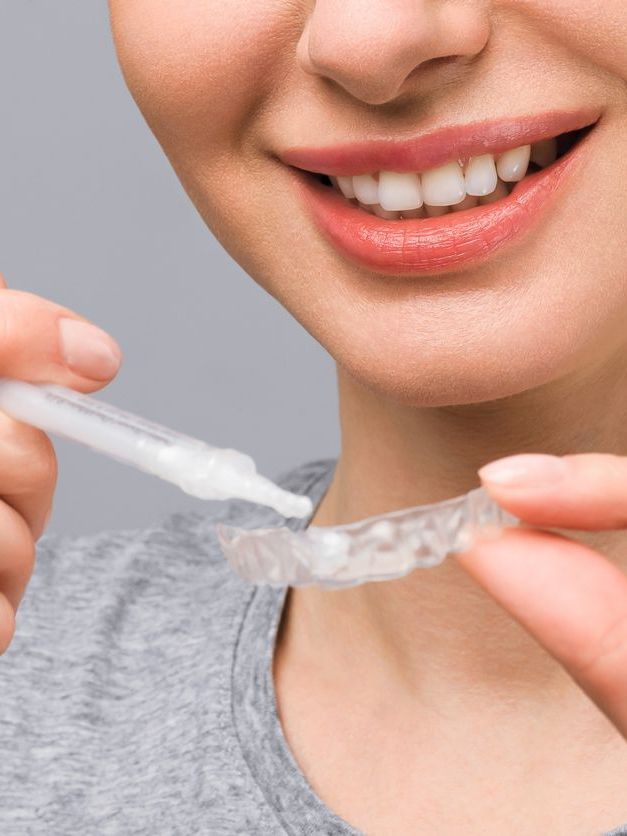 A woman is holding a tooth whitening device in front of her teeth.