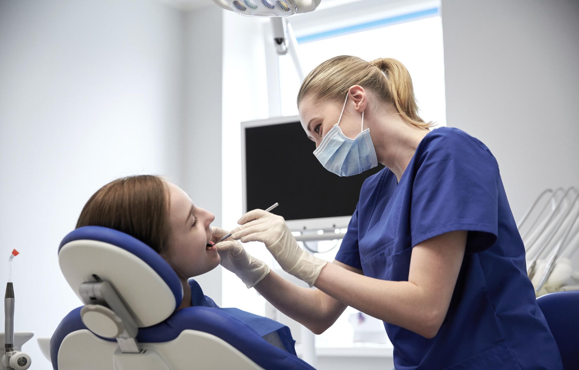 A woman is sitting in a dental chair while a dentist examines her teeth.