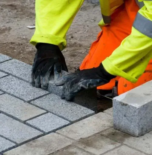 A person wearing gloves is laying bricks on a sidewalk