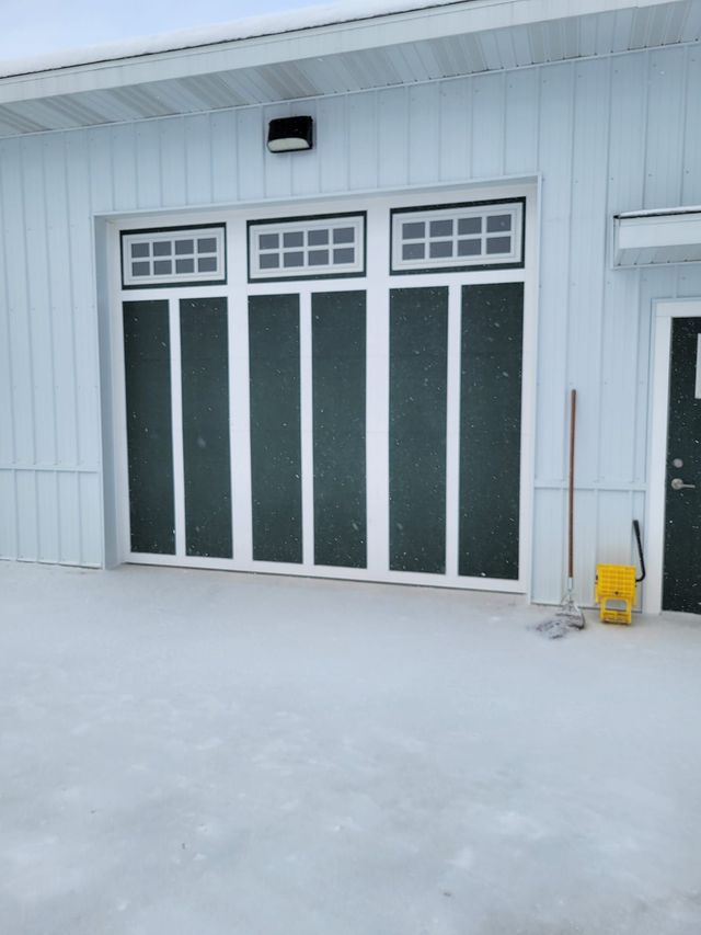 Snowy white house exterior with glass double doors and a small yellow snow shovel by the wall