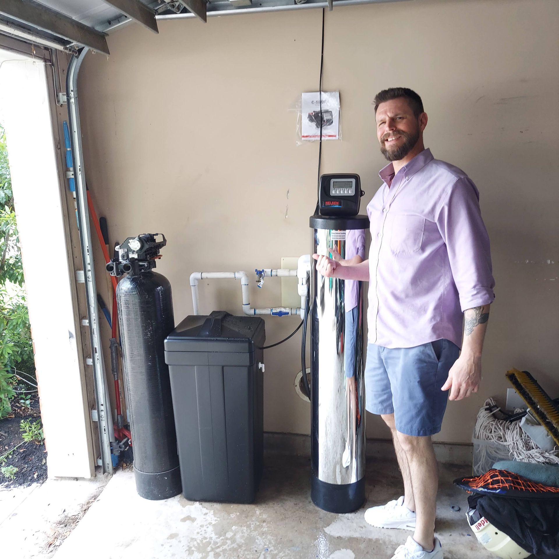 Man smiling next to water filtration system in a garage.
