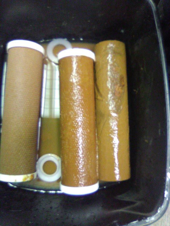 Dirty, clogged reverse osmosis sump-style filters covered in brown sediment, showing how messy and difficult old-style RO filter changes are and why they often cause leaks.