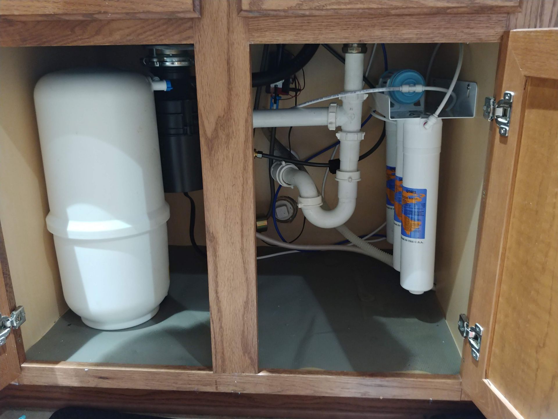 Under-sink Platinum Series Omnipure reverse osmosis system with quick-change filters installed professionally with clean, organized tubing.Tight fit, it cannot touch the garbage disposal.