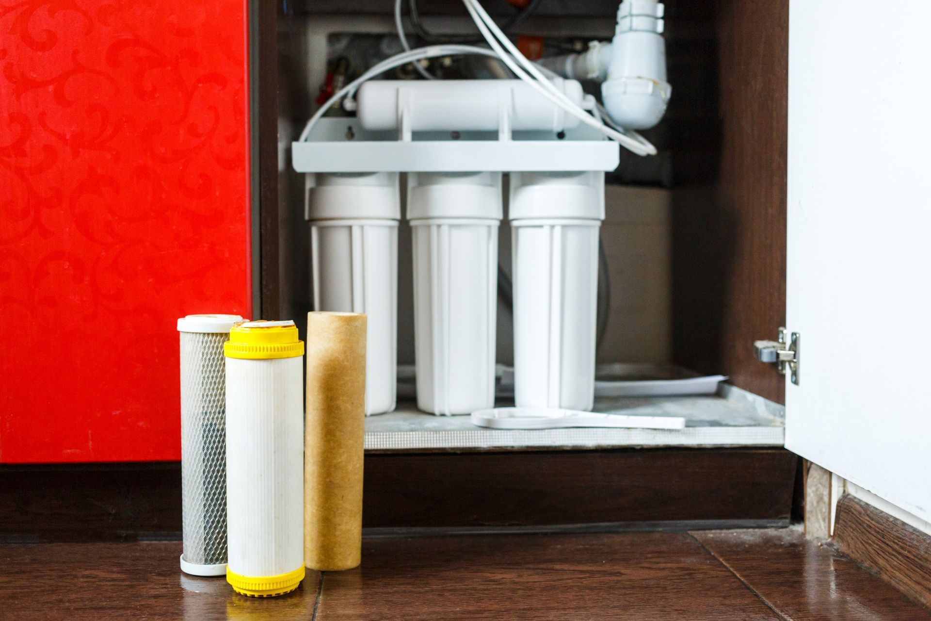Water filter system with replacement cartridges in an open cabinet.