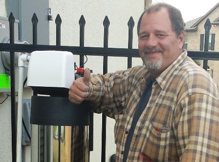 Wayne Mathews standing next to a finished whole-house water filtration and softening system installation in Katy, Texas, giving a thumbs-up