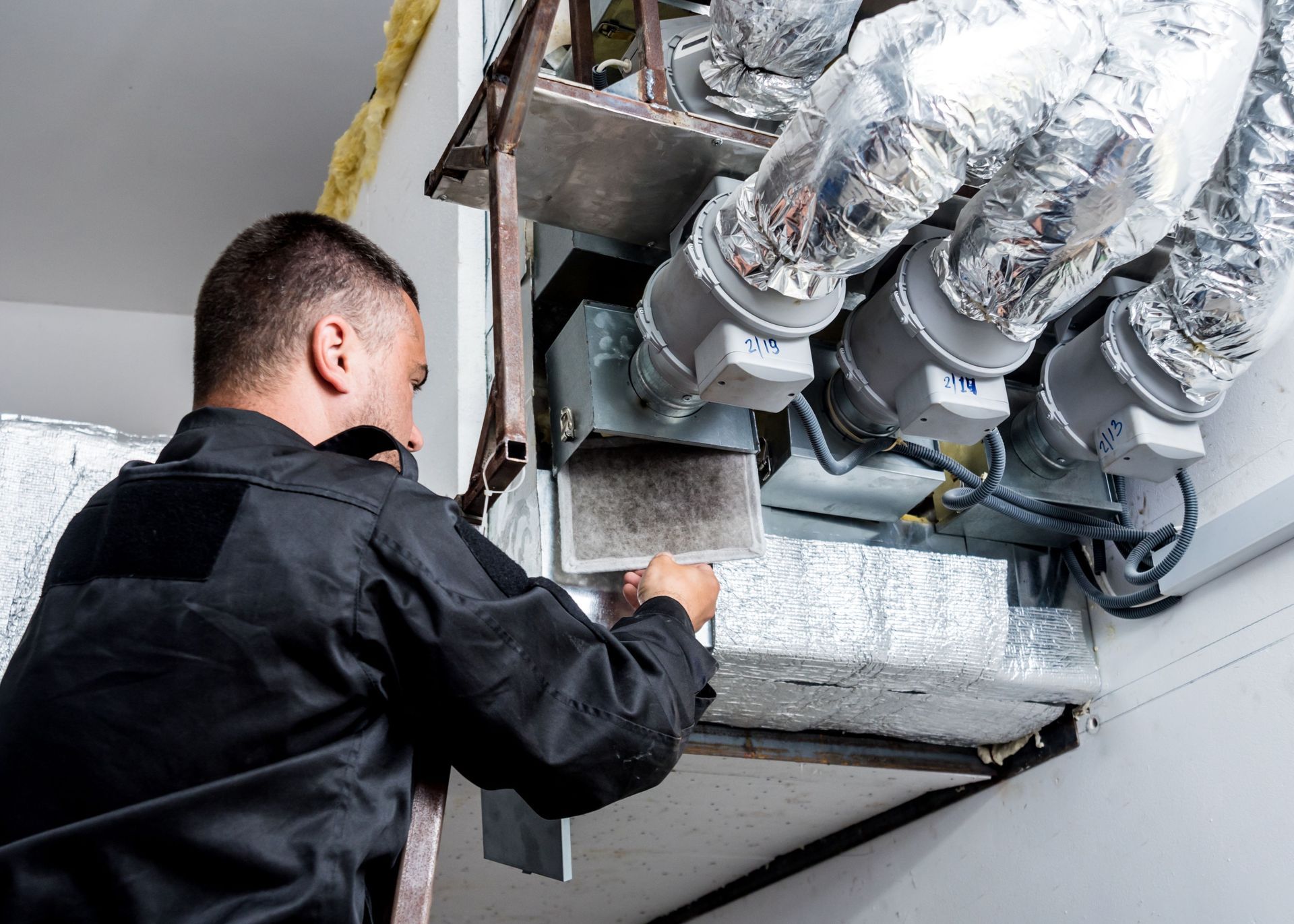A man is working on a ventilation system in a building.