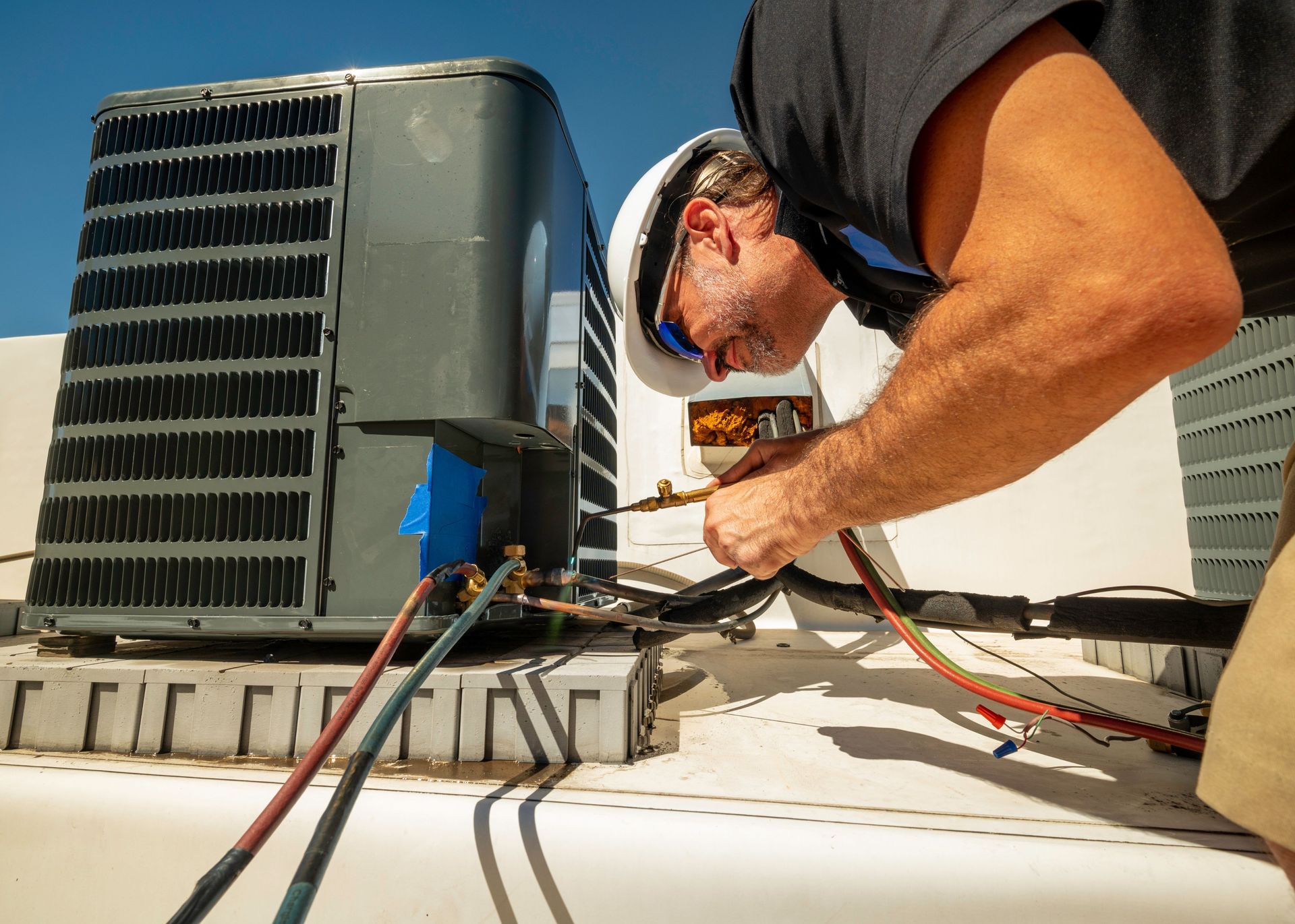 A man is working on an air conditioner on the roof of a building.