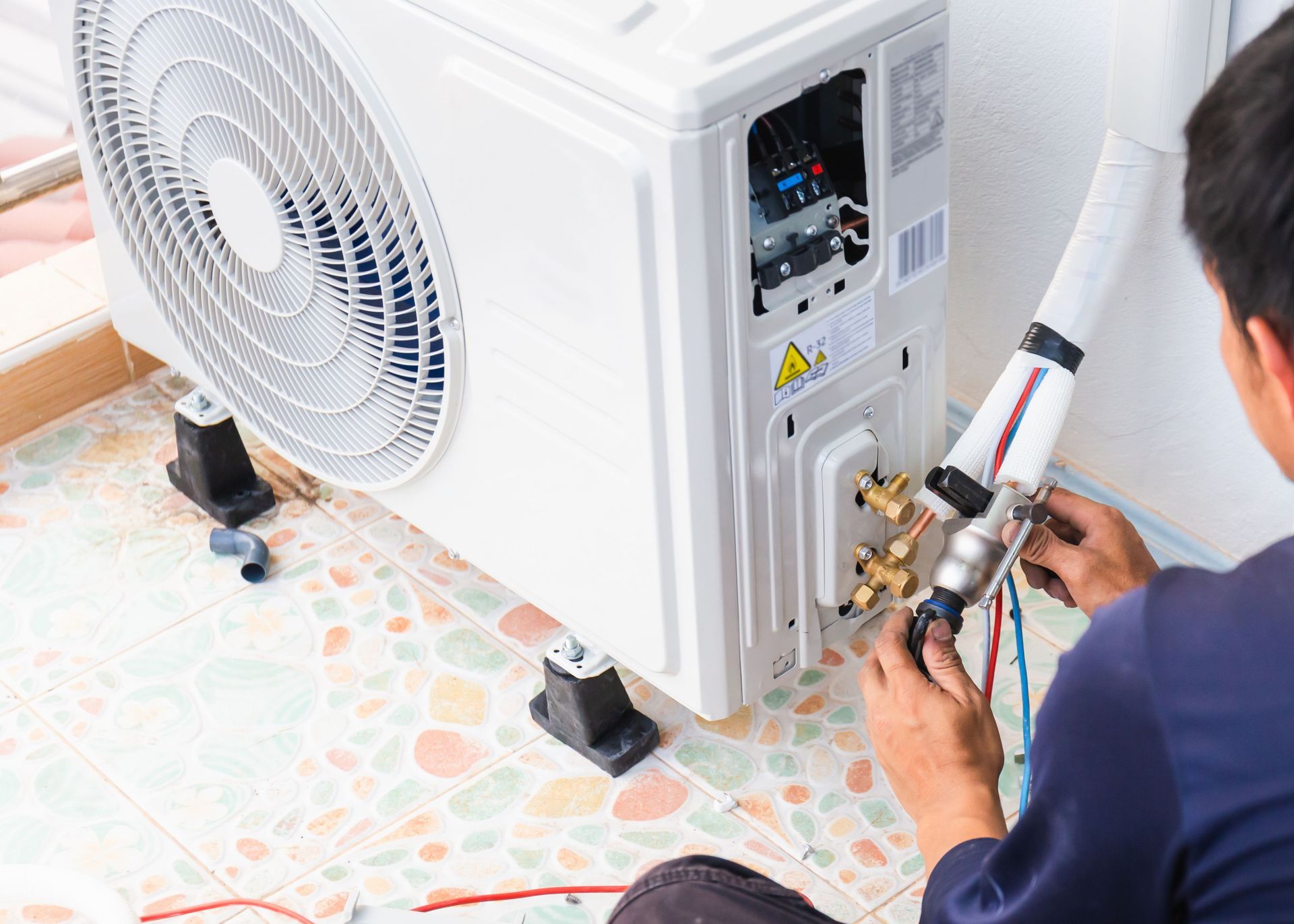 A man is sitting on the floor fixing an air conditioner.