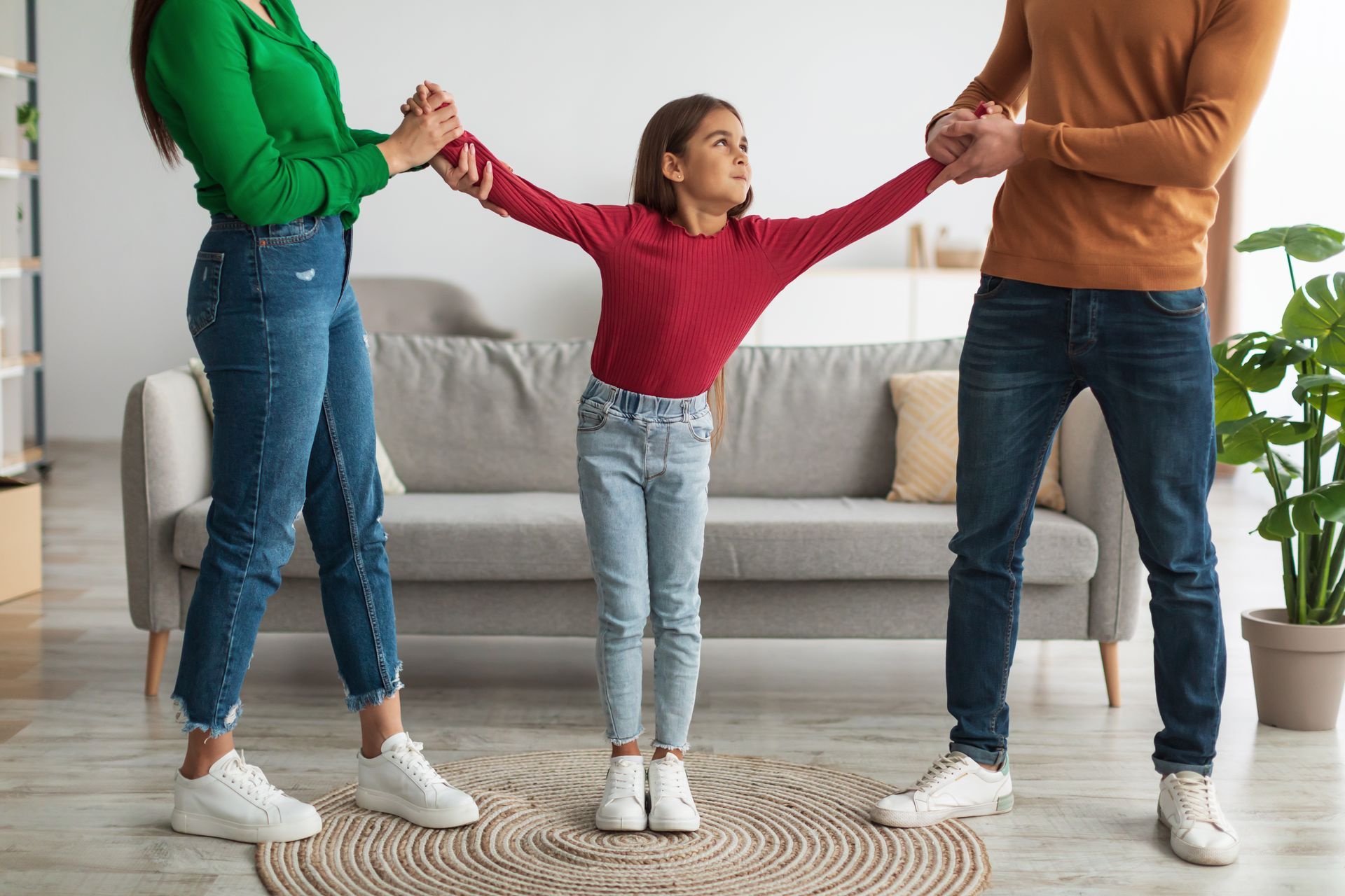 A child stands between two adults, each holding a hand, in a living room.