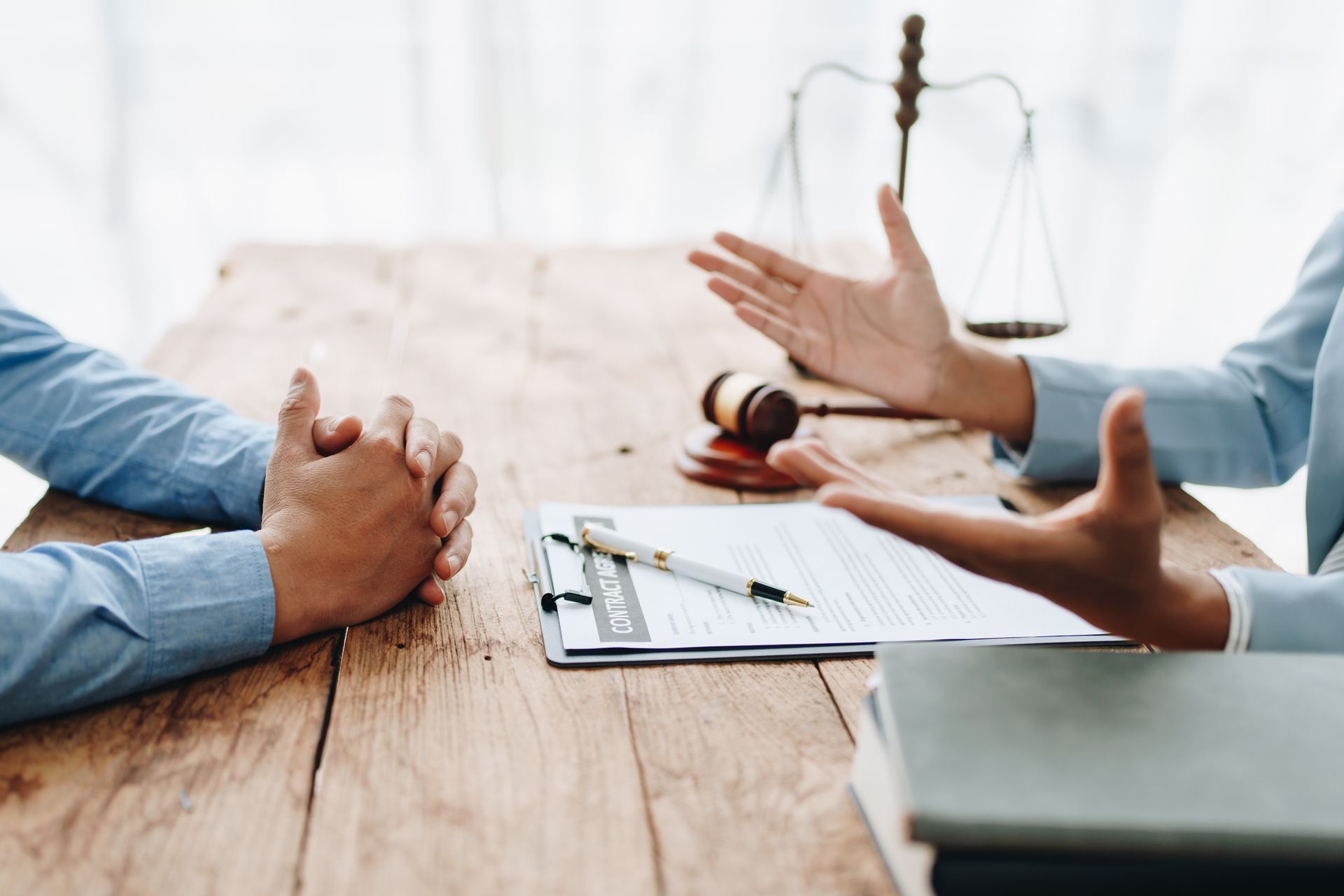 Lawyer gesturing to a client at a wooden table with documents, a gavel, and scales of justice.