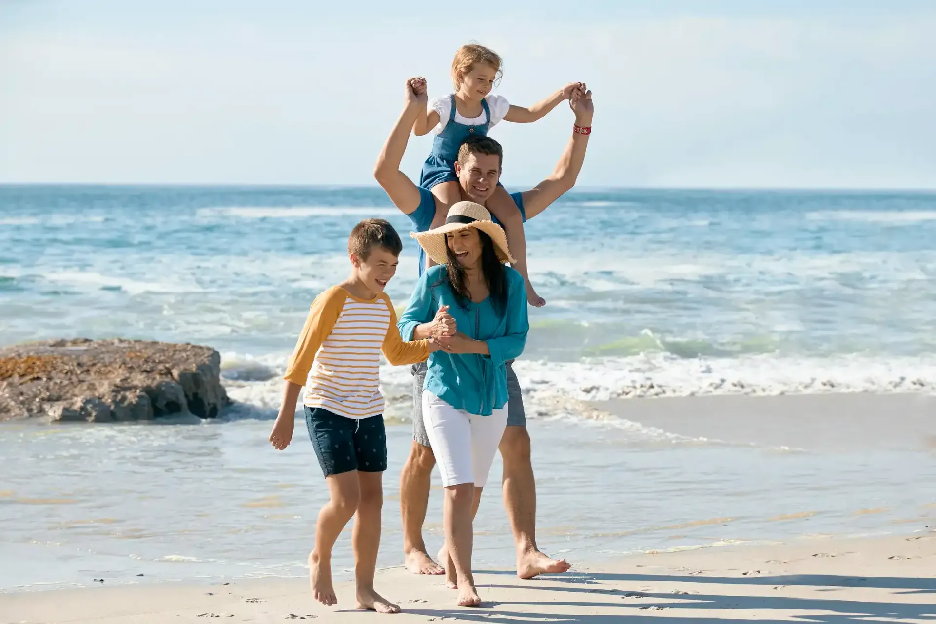 A family is walking on the beach with their children on their shoulders.