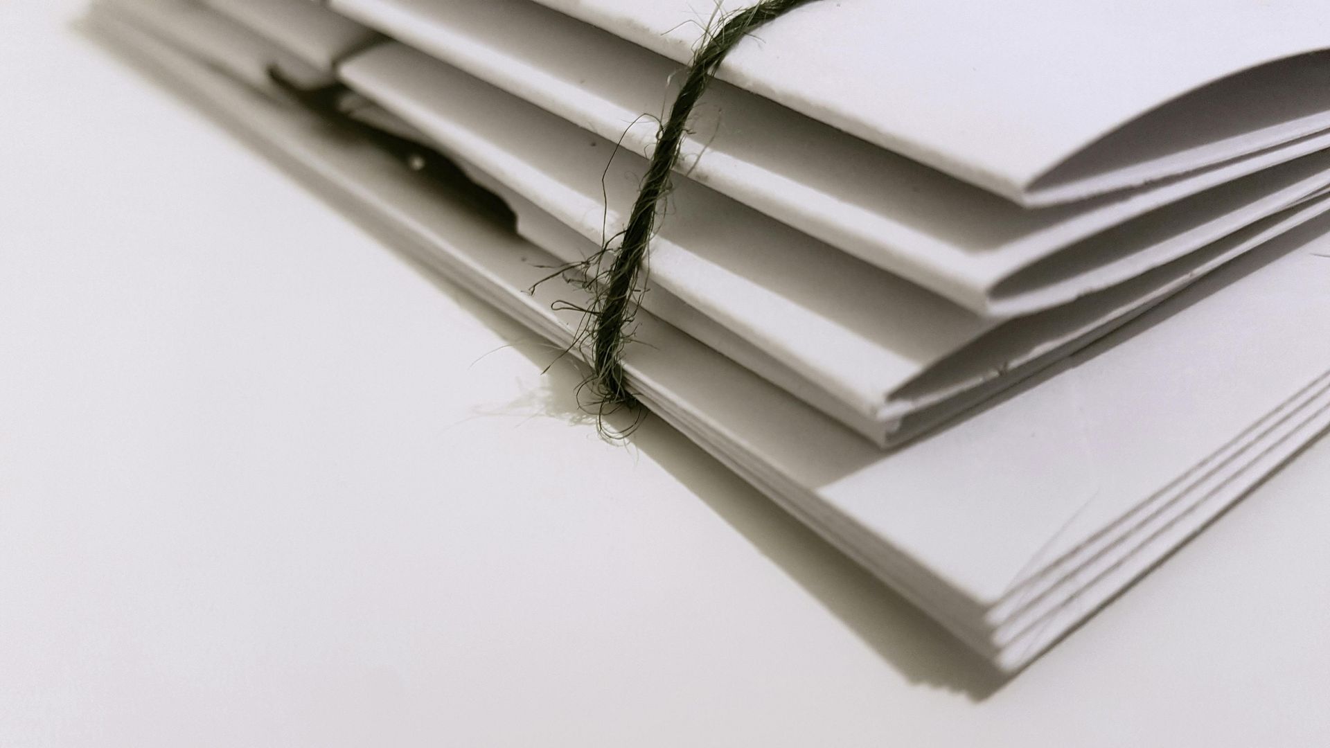 Stack of white papers bound with a black string, resting on a white surface.