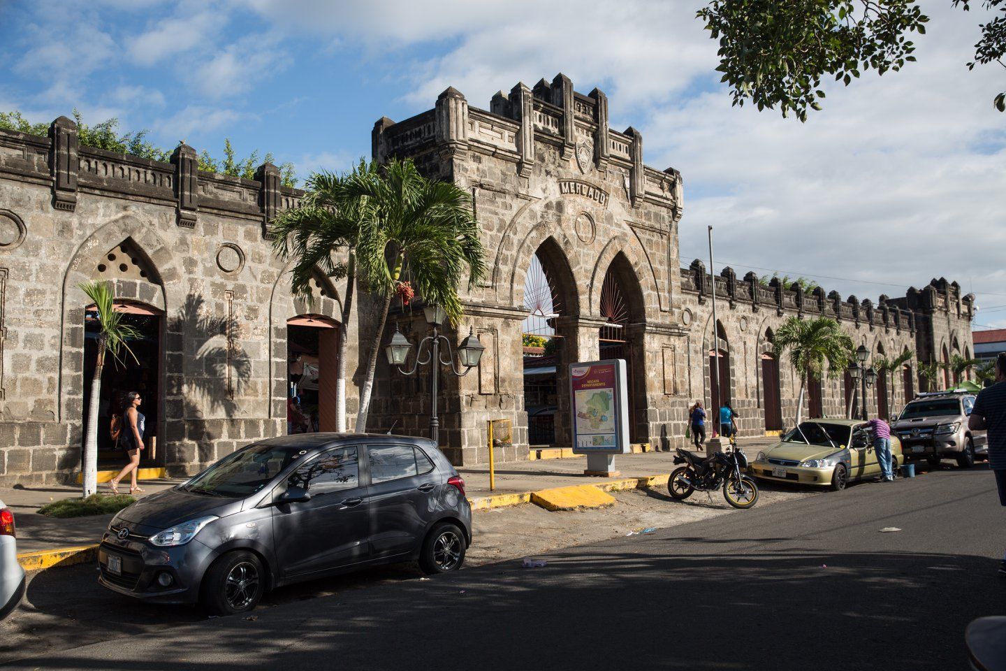 A row of cars are parked in front of a stone building.