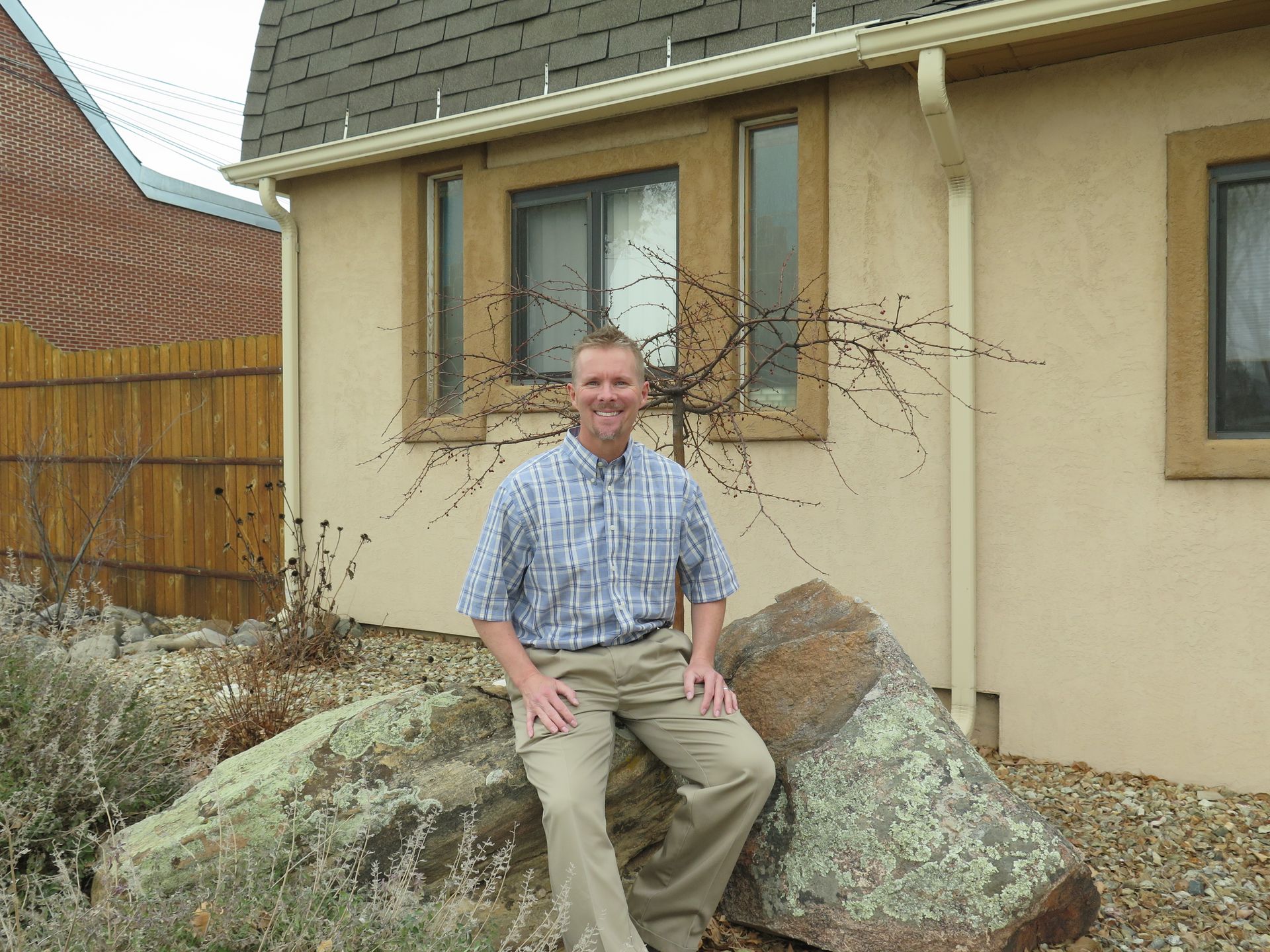 A man is sitting on a rock in front of a house