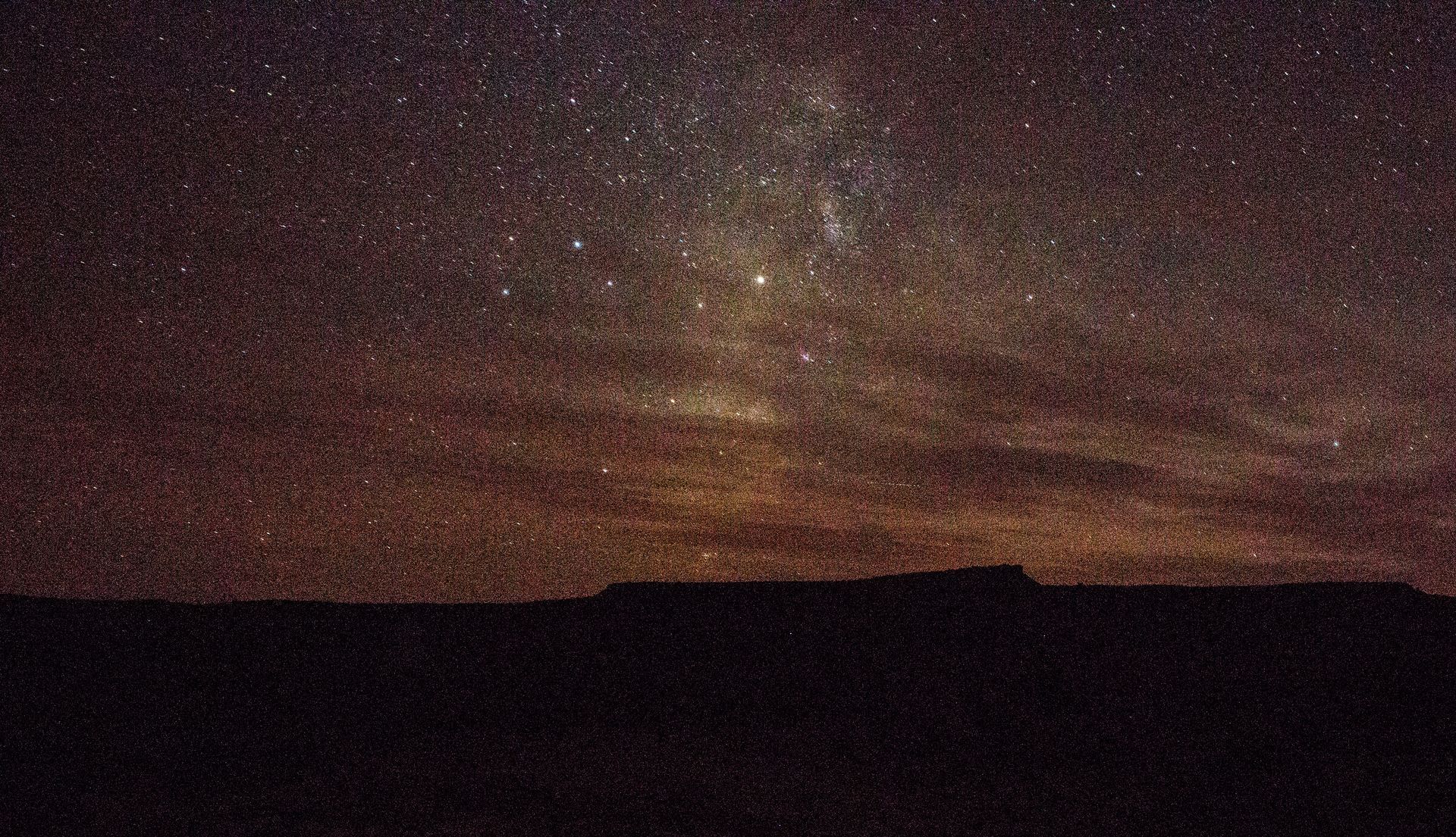A night sky filled with lots of stars over a desert landscape.