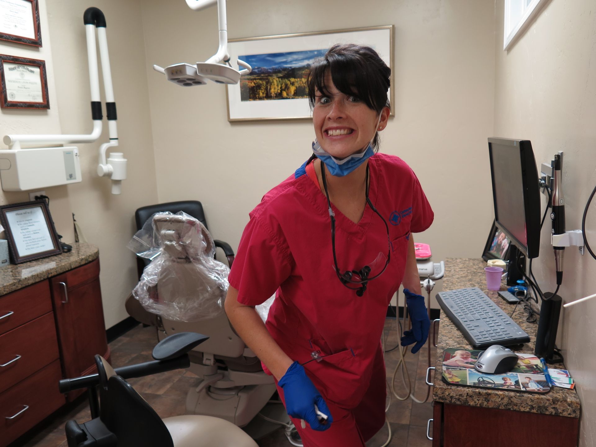 A woman in a red scrub is standing in a dental office.