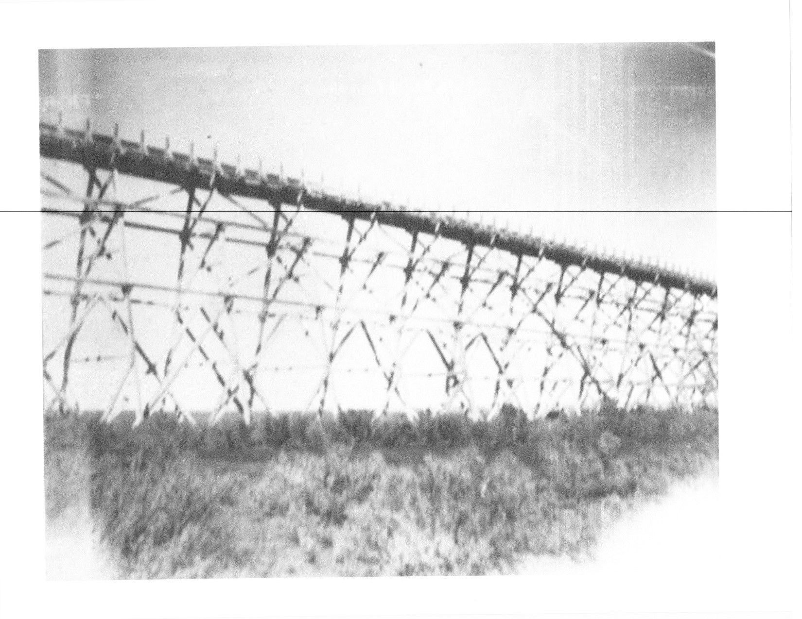 A black and white photo of a bridge in the middle of a field.