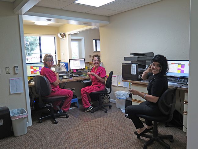 Three women in scrubs are sitting at desks in an office.