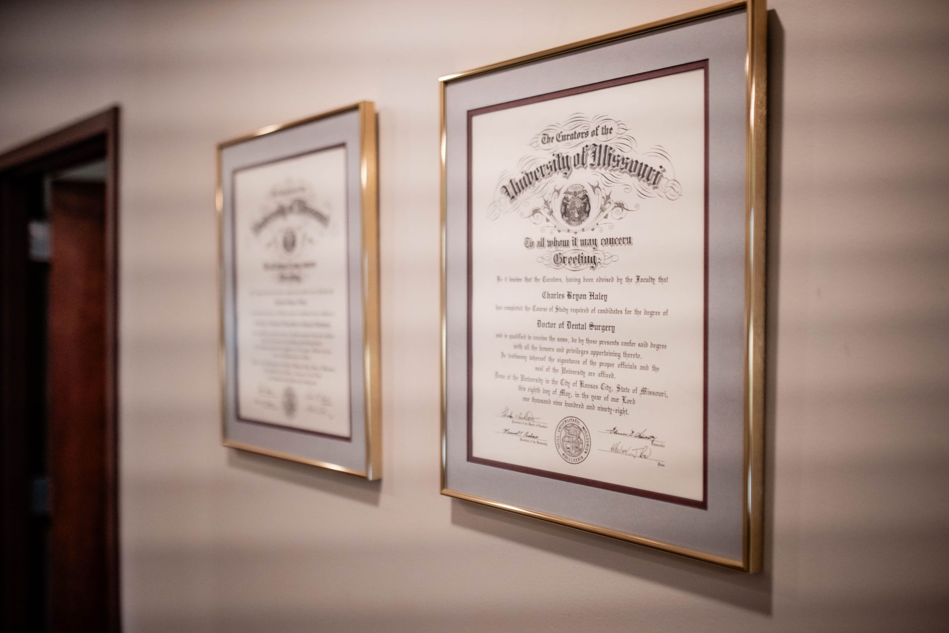 Two framed diplomas are hanging on a wall next to a door.