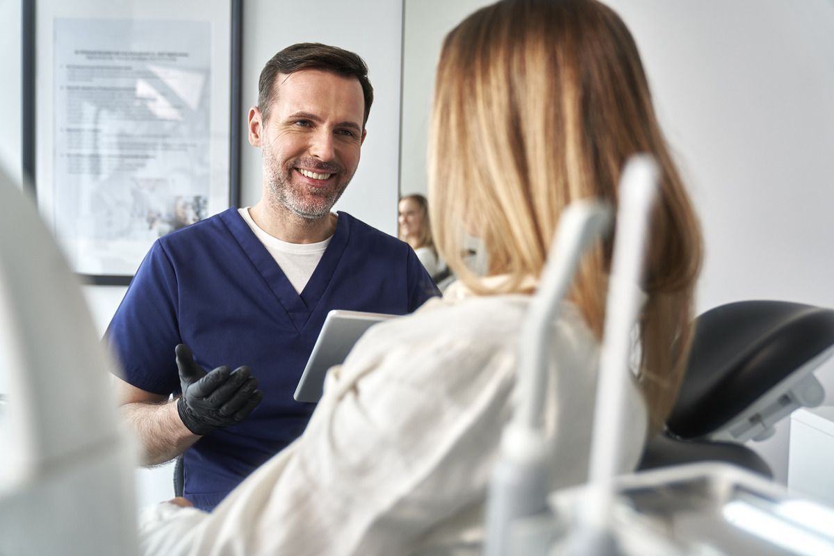 A dentist is talking to a patient in a dental chair.