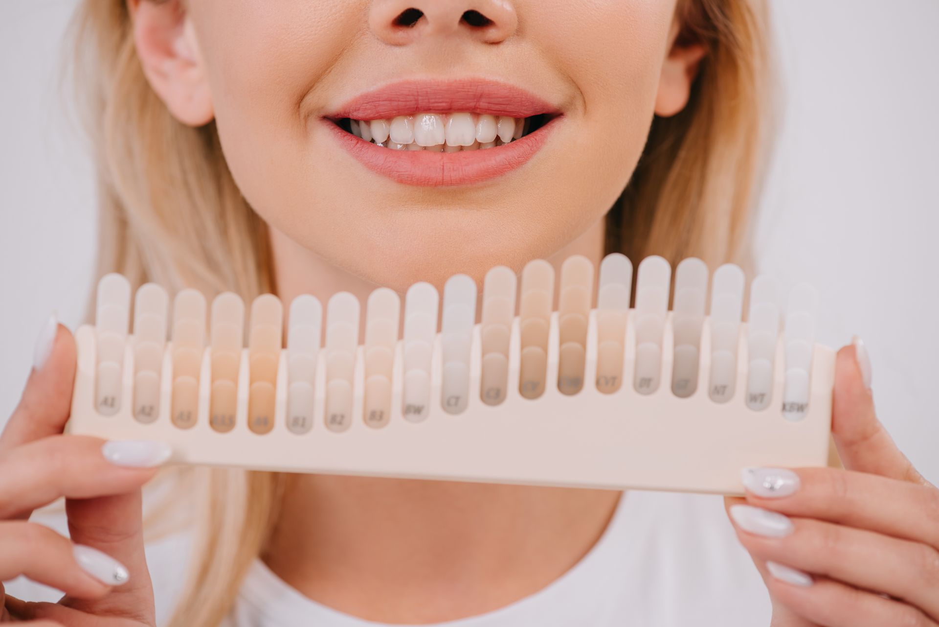 A woman is holding a tooth color chart in front of her mouth.