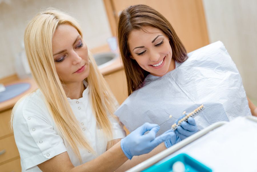 A woman is sitting in a dental chair while a dentist examines her teeth.