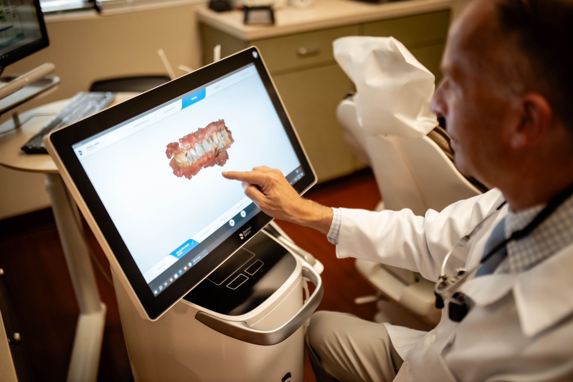 A dentist is pointing at a computer screen in a dental office.