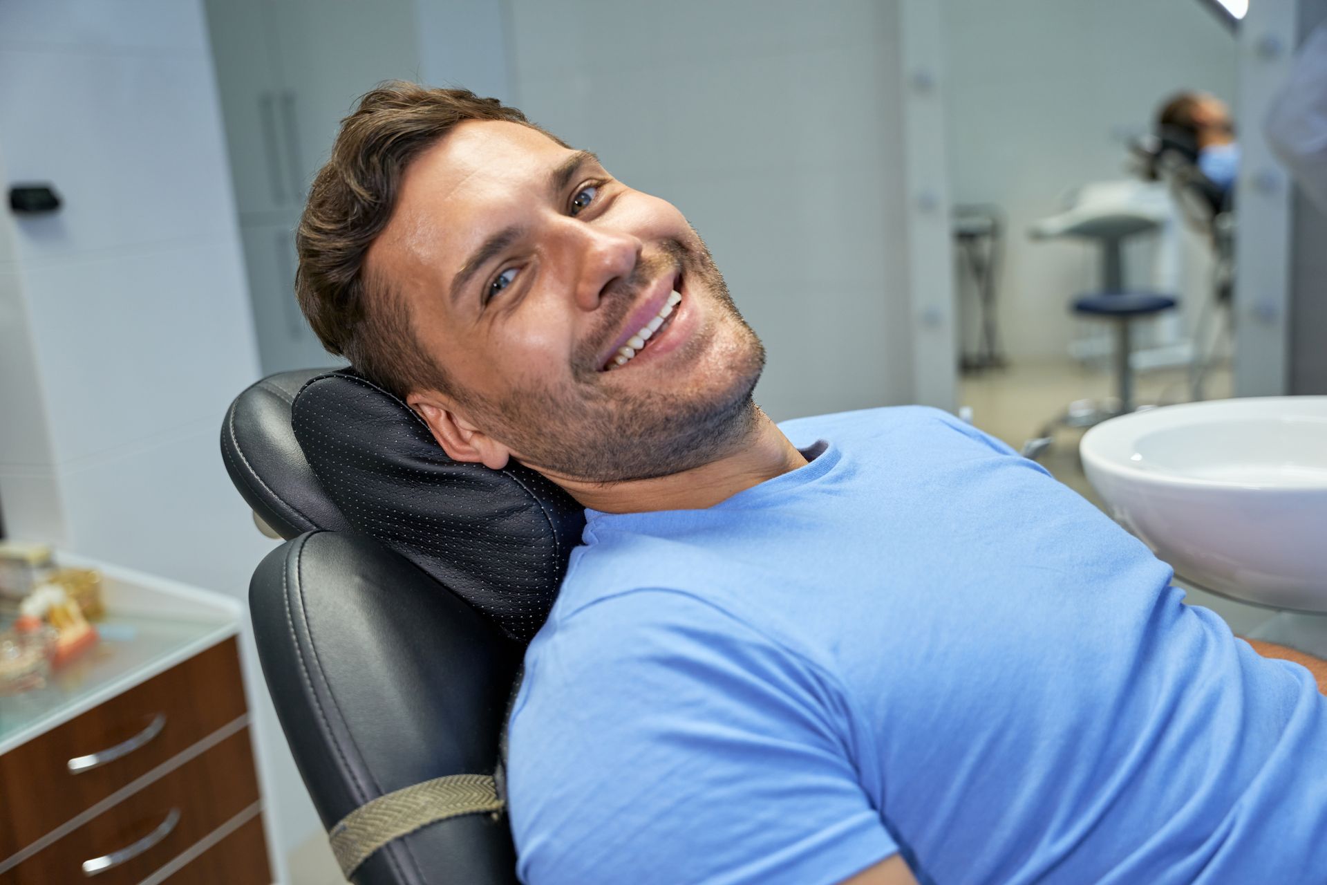 A man is smiling while sitting in a dental chair.