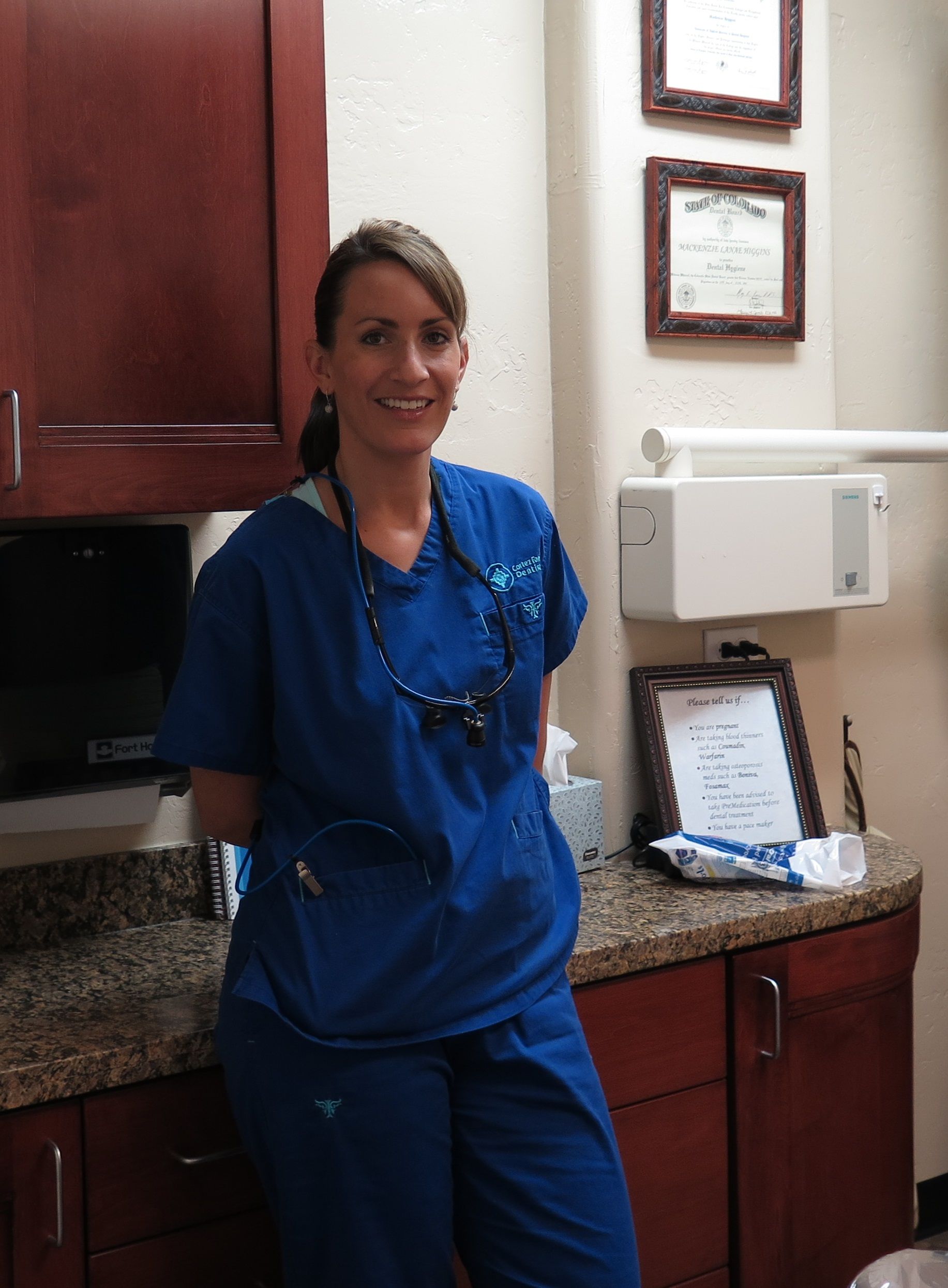 A woman in blue scrubs is standing in a dental office.