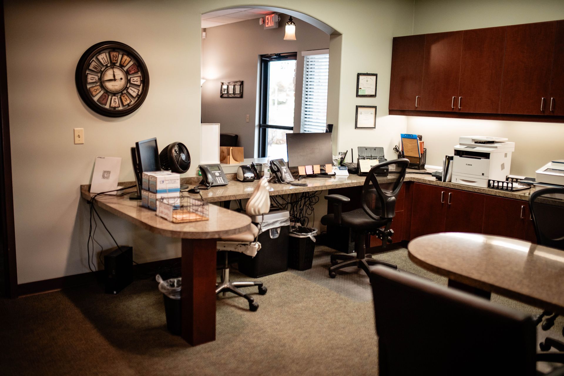 There is a clock on the wall above the desk in the office.