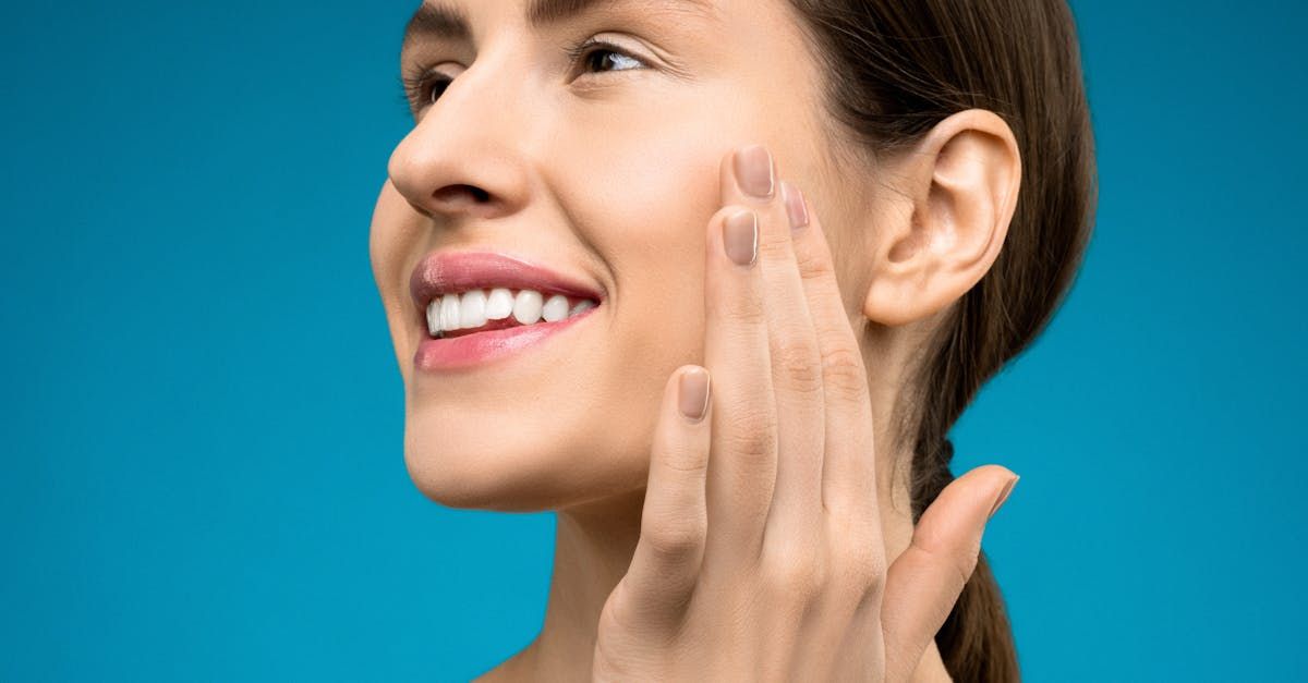 A woman is smiling while touching her face with her hand.