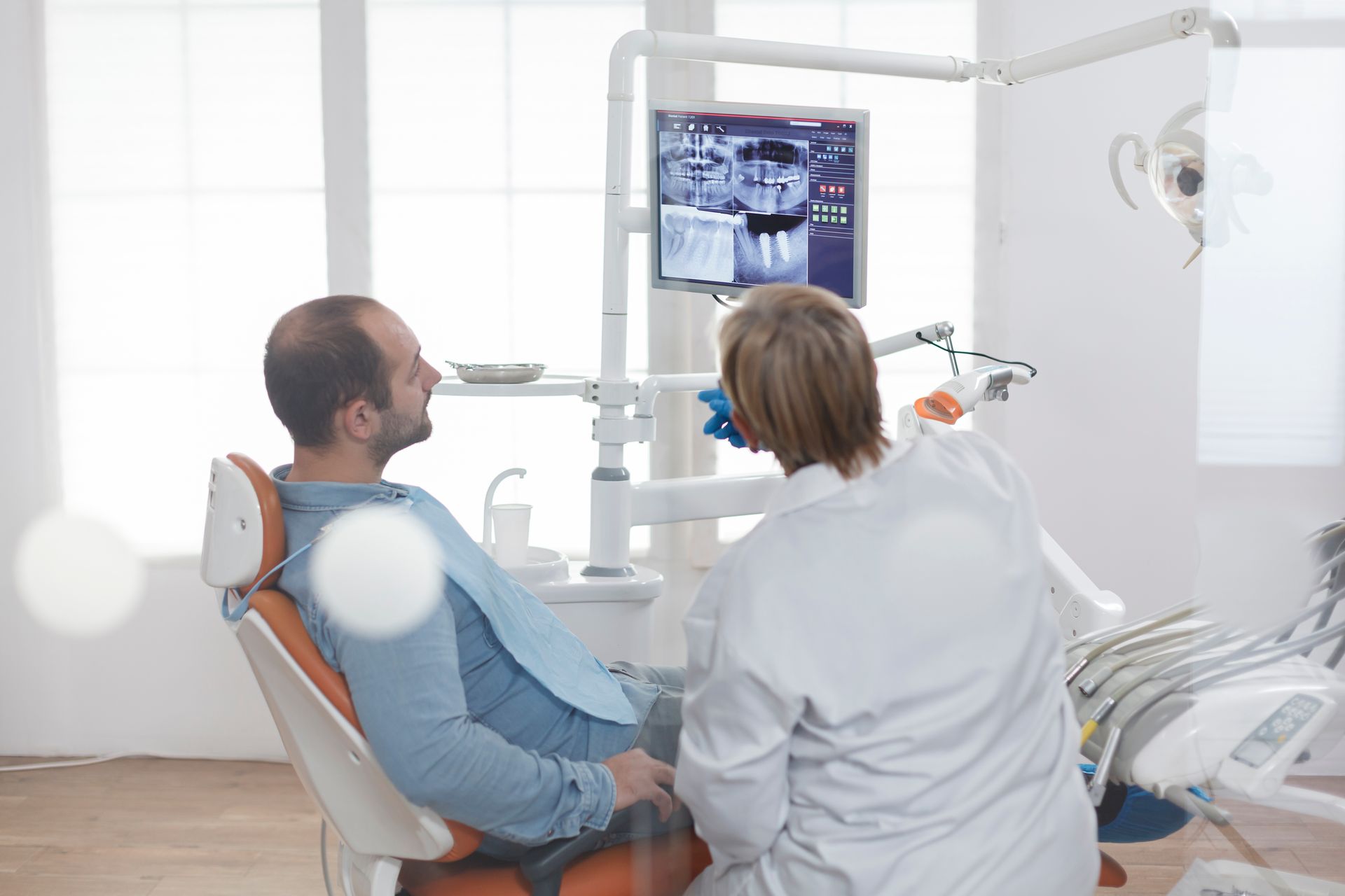 A man is sitting in a dental chair talking to a dentist.