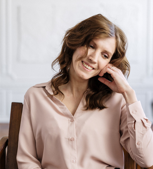 A woman in a pink shirt is sitting in a chair and smiling.