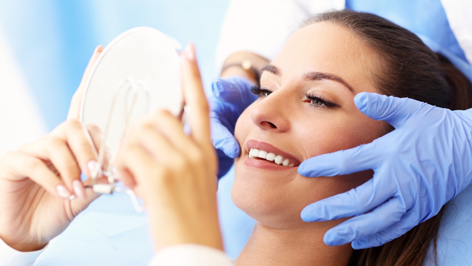 A woman is looking at her teeth in a mirror at the dentist.