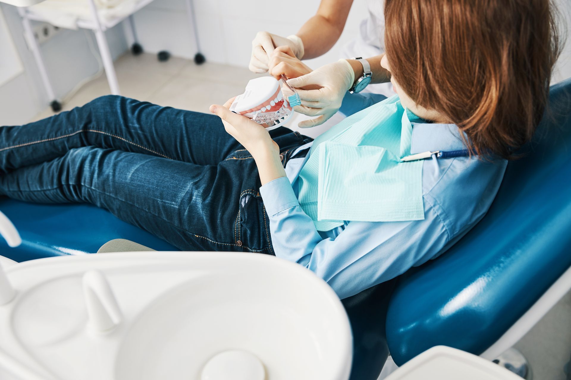 A woman is laying in a dental chair while a dentist examines her teeth.