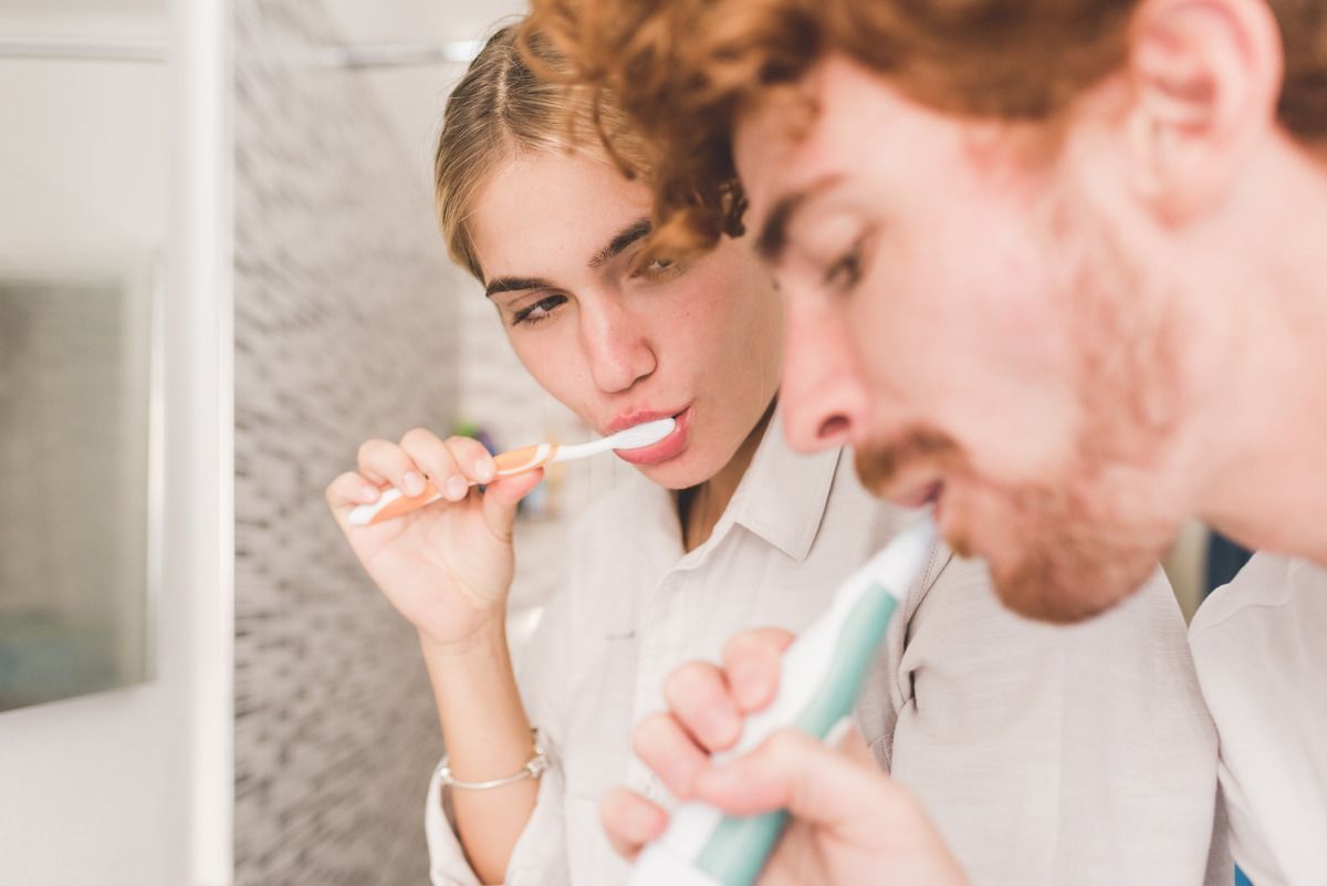 A man and a woman are brushing their teeth in front of a mirror.