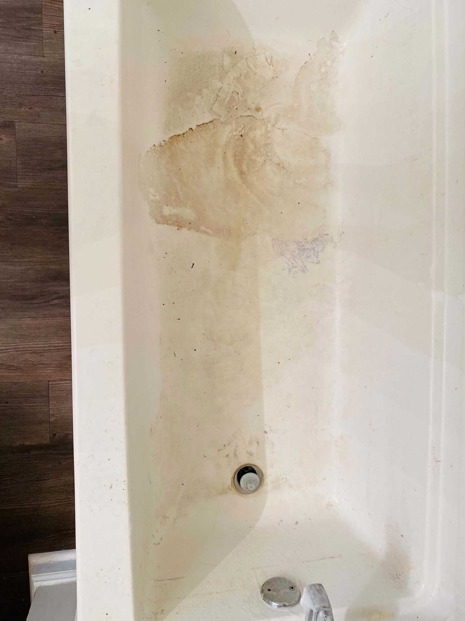 Dirty white bathtub interior with brown stains, visible drain, and faucet.